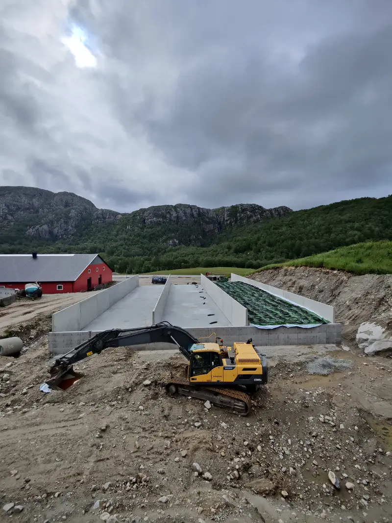 Gravemaskin ved den ferdige plansiloen, med rød driftsbygning i bakgrunnen