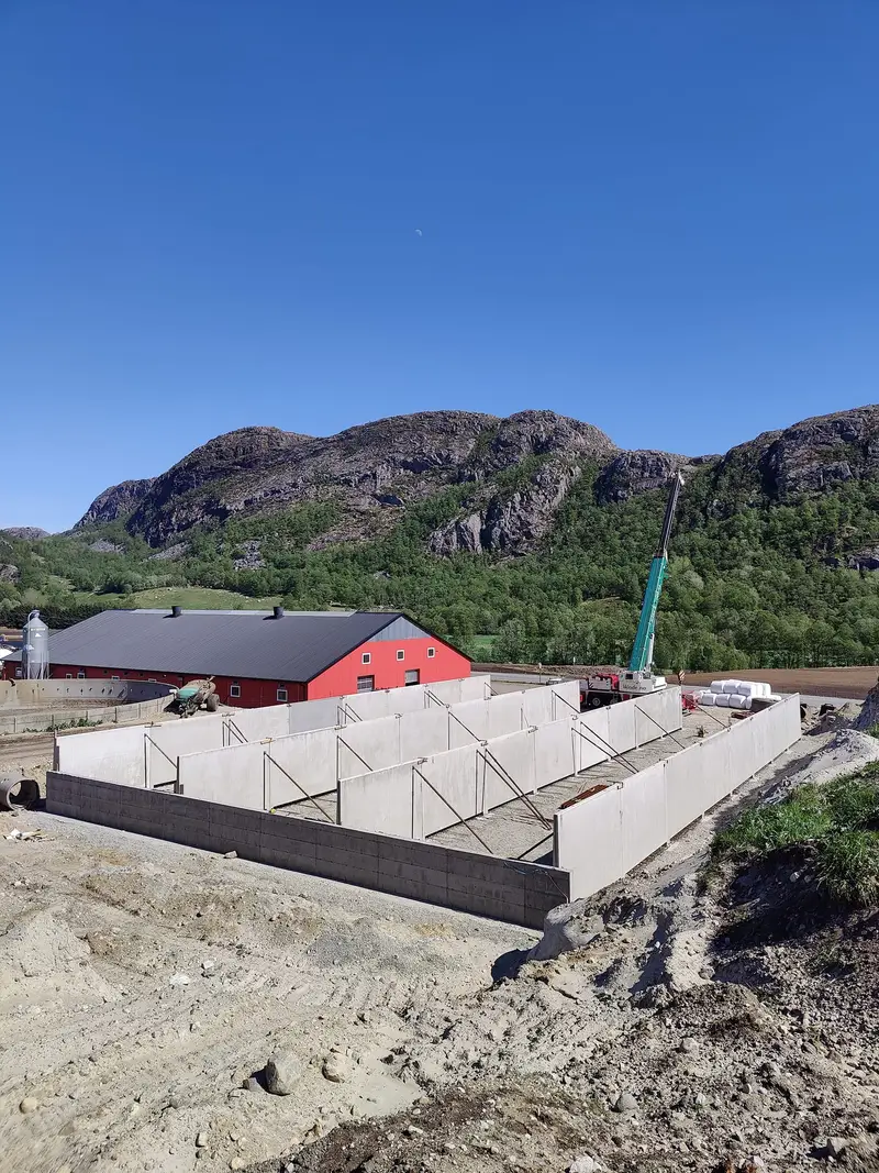 Betongveggene til plansiloen satt opp ved en rød driftsbygning, med fjell i bakgrunnen